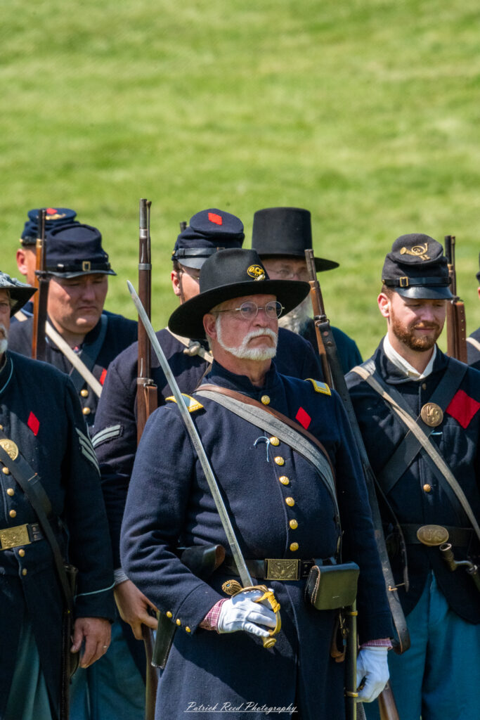 Union soldiers standing in formation, dressed in their iconic blue uniforms, ready for duty. Their expressions are serious and focused, reflecting the discipline and camaraderie of the unit. The scene captures the spirit of the Union Army during the Civil War, showcasing their readiness for battle.